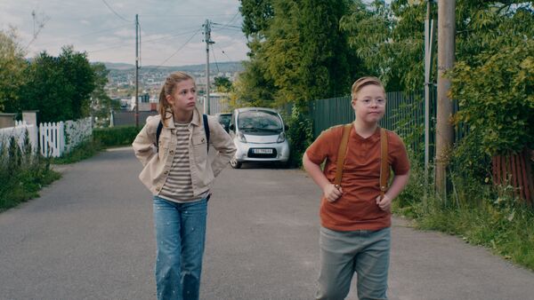 A pre-teen girl and a boy walk along a street in Norway