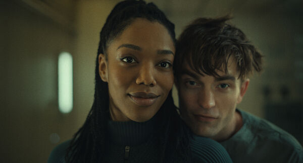 A man and woman in futuristic outfits smile in a mirror.