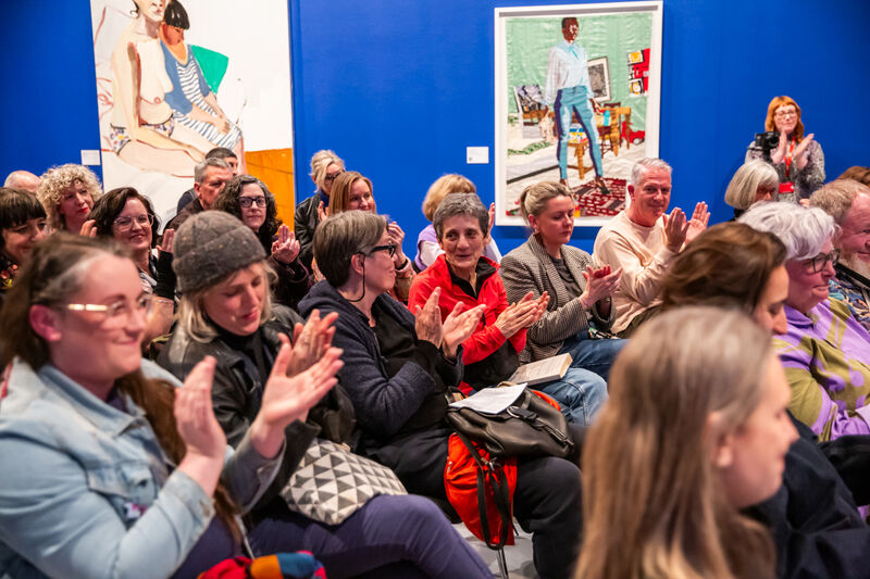 A busy audience clapping in a seated gallery space