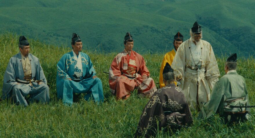 A group of samurai in different coloured outfits sit on a green hill.