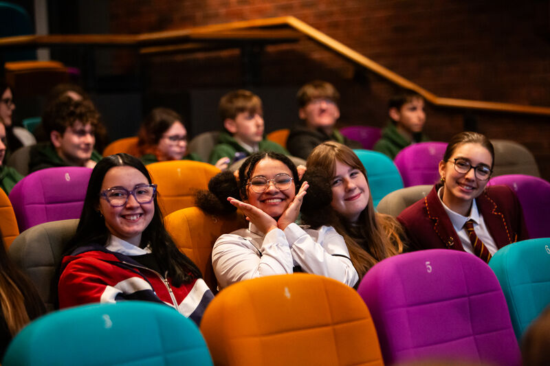 Four teen girls sit in colourful seats at DCA Cinema.
