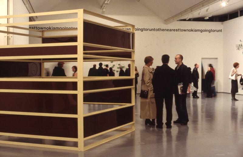 People stand next to a large wooden structure in the shape of a square, in DCA Galleries.