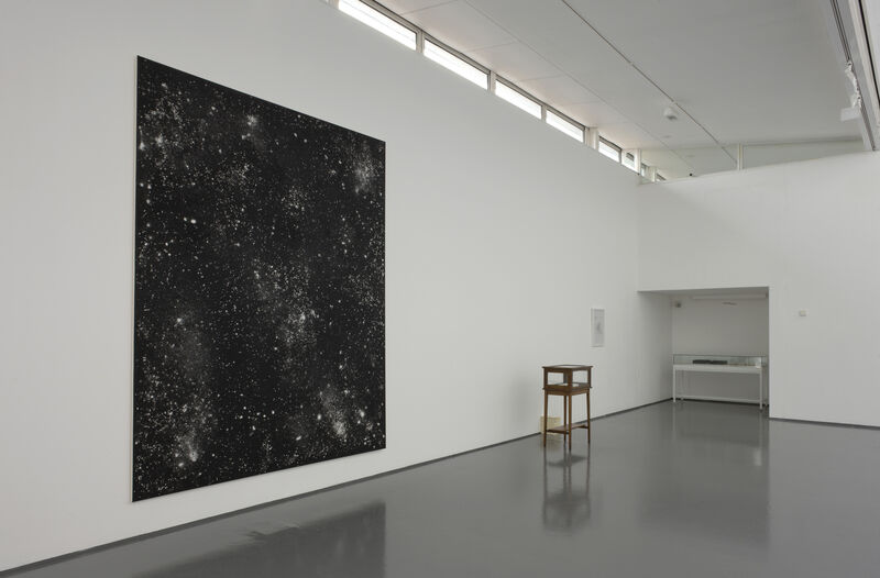 From Timecode exhibition. A black canvas hangs on DCA Gallery walls. It is speckled with white paint that looks like stars.