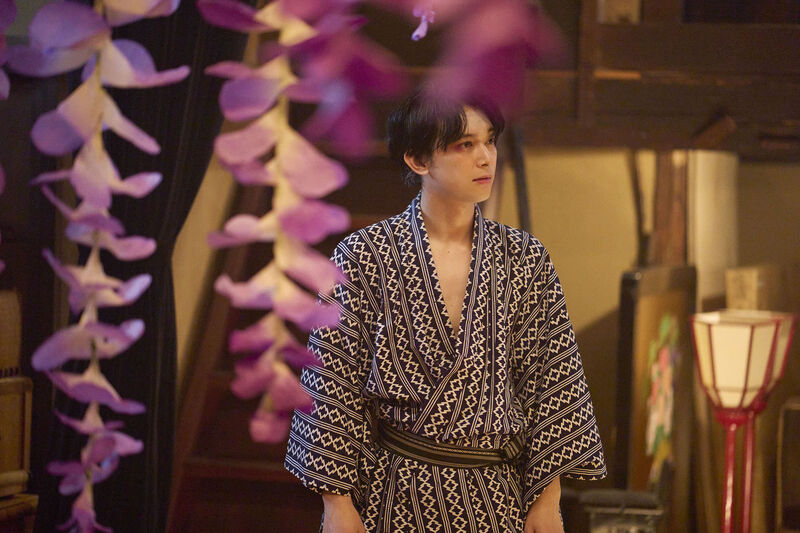 A man in a kimono, surrounded by hanging flowers.