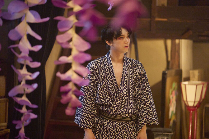 A man in a kimono, surrounded by hanging flowers.