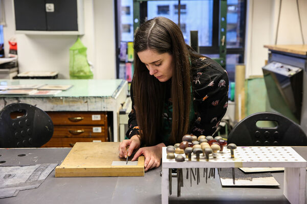 Person using lino cutting tools to make a design on a piece of lino