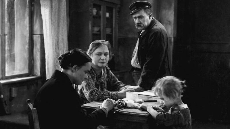 A black and white image of three people around a table 
