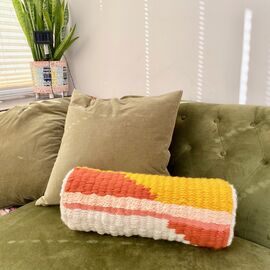 Orange, yellow and cream woven bolster cushion on a green sofa