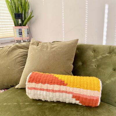 Orange, yellow and cream woven bolster cushion on a green sofa