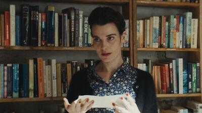 A woman stands in front of a book shelf looking at a note.