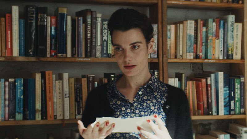A woman stands in front of a book shelf looking at a note.