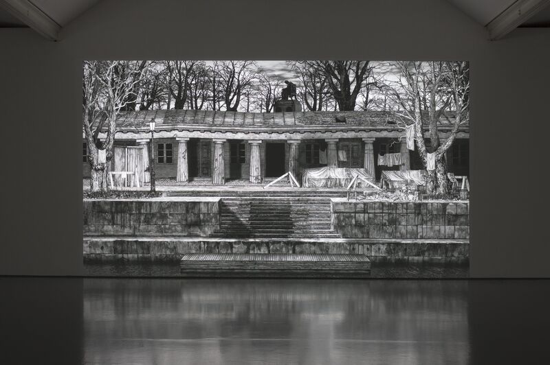 From IC-98' exhibition. A projection shows a monochrome, hand-drawn image of a ruined building with Greek columns. The building is surrounded by trees.