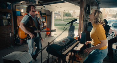 A man and a woman play the keyboard and play guitar together in a garage together