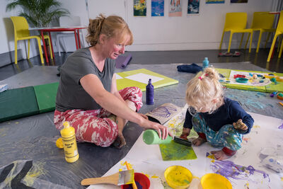 Parent and child making art on a big sheet of paper using paint and a roller
