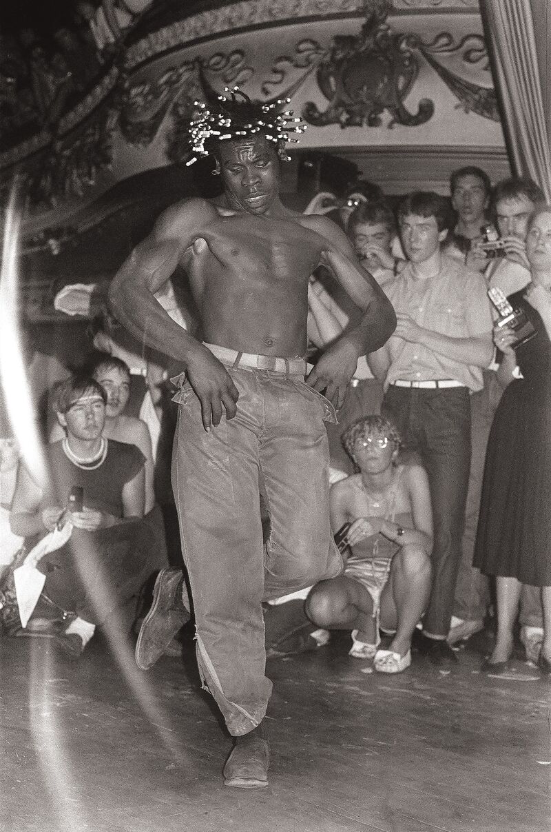 Shirtless man with beads in his hair dances.