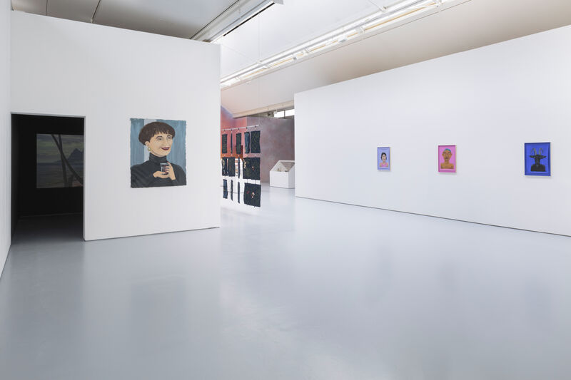 Installation image showing a the entrance to a booth where a film plays, and four paintings. 