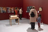 A red gallery space with people looking at works on the wall