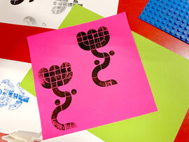 Lego prints of flowers in black ink on pink paper