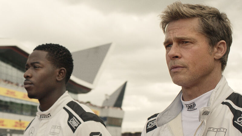 Two men in white formula 1 racing uniforms stand next to each other.