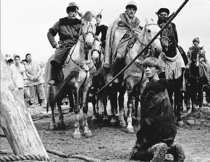 A young man kneels before men on horseback