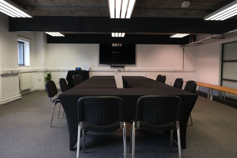 A  meeting  room with a table in the middle and chairs around it facing a screen. a b