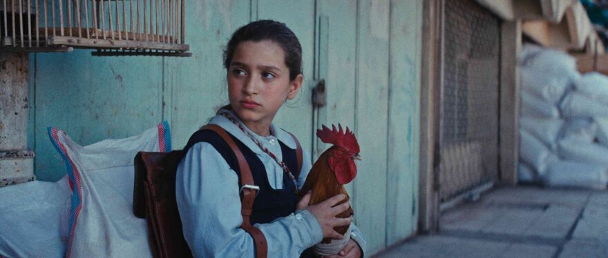 A young girl in a school uniform sits outside holding a chicken