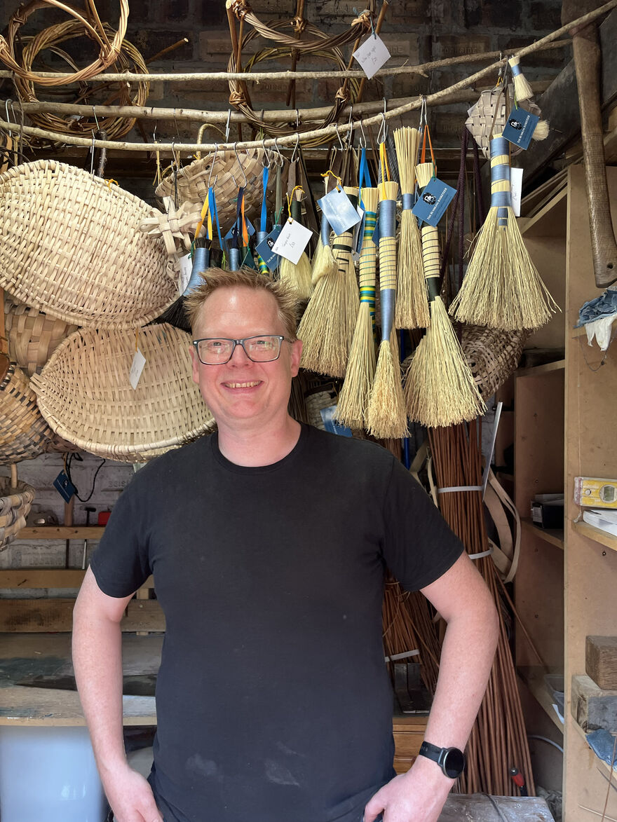Man with glasses standing in front of a display of brushes and baskets