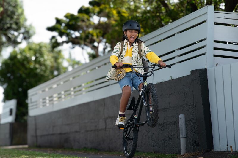 A young Maori tween does a wheelie on their bike.