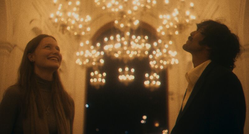 A young woman and a young man smile up in wonder in a beautifully lit chamber