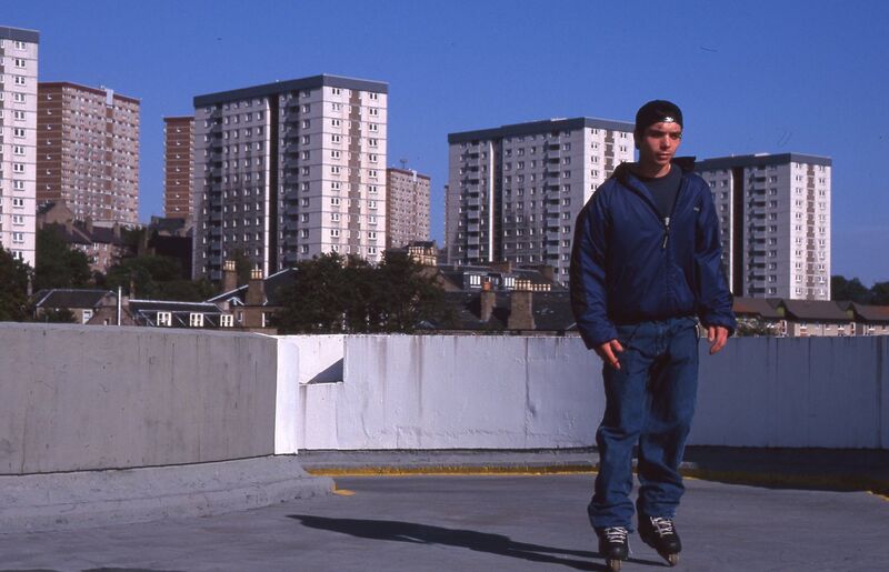 From Roderick Buchanan's exhibition at DCA. A person skateboards in an empty parking lot in Dundee. The multi-story flats can be seen in the background.