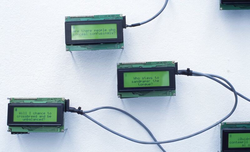 Small motherboard machines with messages on them hang on a white gallery wall.