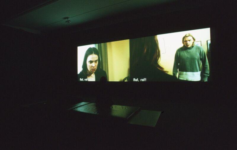 A projector shows a film with three people on it, who look angry.