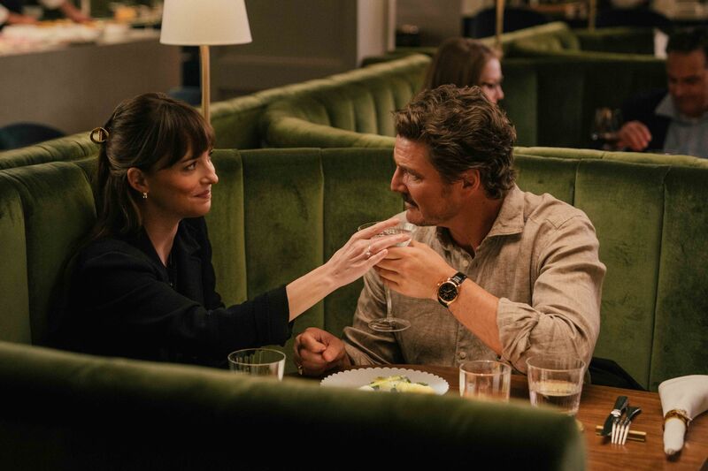 A man and a woman sit in a restaurant booth together. The woman holds the man's martini glass.