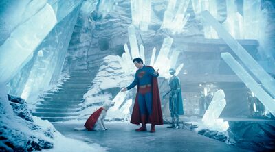 Superman talks to a dog wearing a cape and a robot in an ice cave.