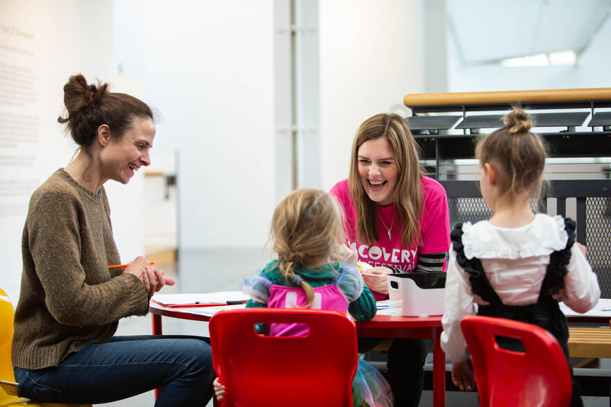 Two children and two adults sitting at a table doing creative activities, laughing. 