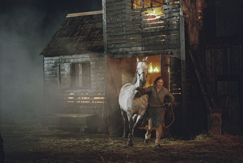 A man and a horse run out of a burning barn.