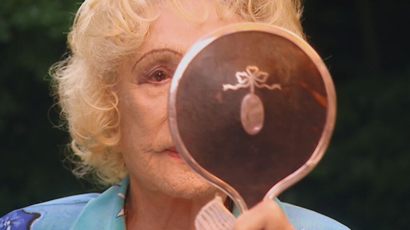 An elderly Leni Riefenstahl looks into a hand-held mirror.