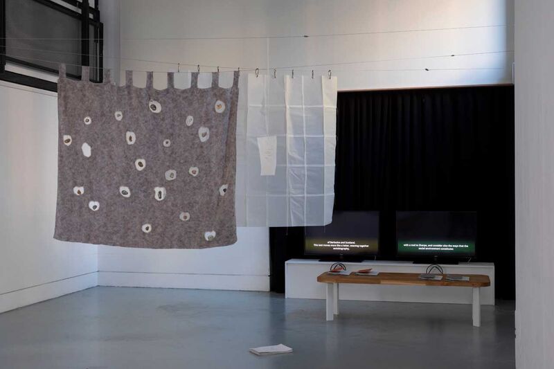 A gallery space with an artwork of fabric hanging down and a large screen  