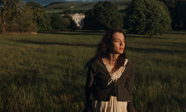 A dark haired woman on a moor in front of a beautiful house.