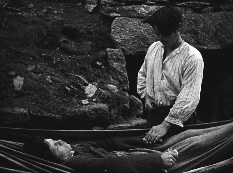 A man holds the hand of a woman lying unresponsive, her eyes closed