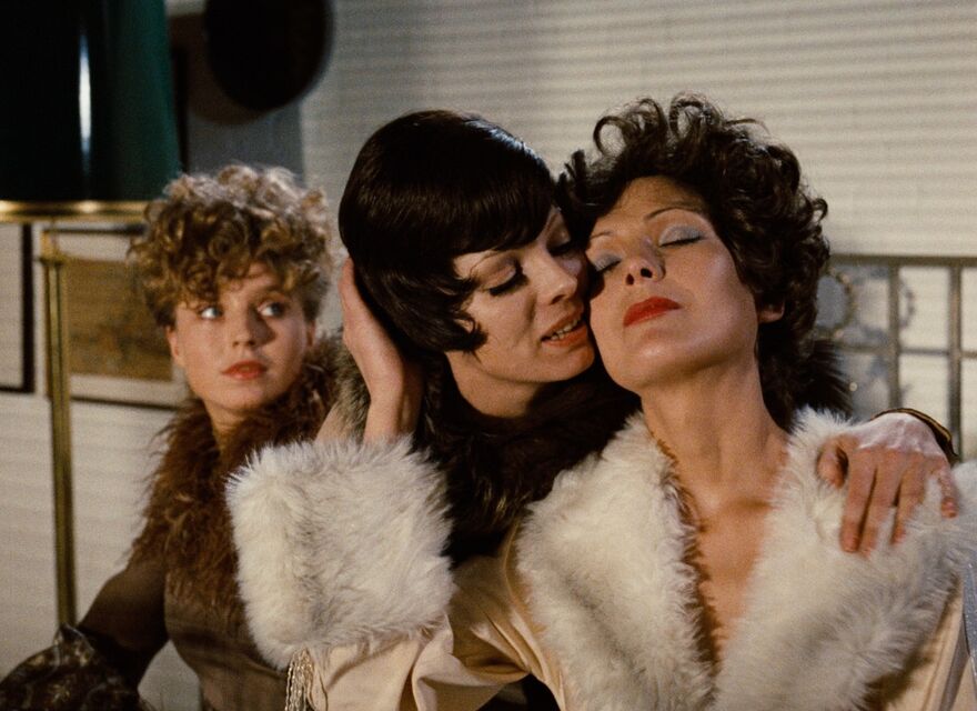 Two women embrace as another looks on.
