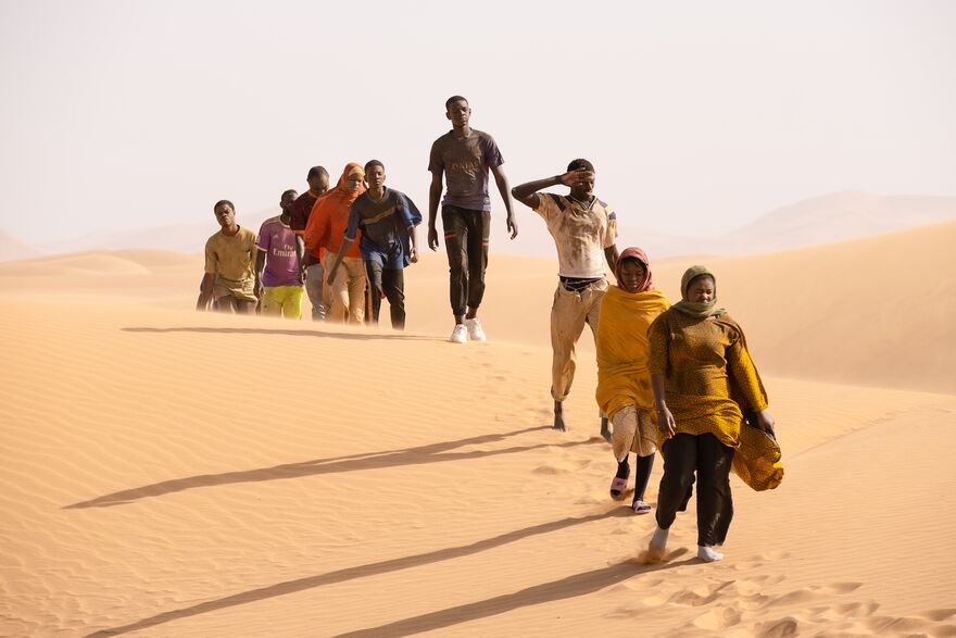 A group of travellers walk over a sand dune in the searing heat