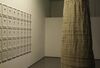 From Navid Nuur's exhibition. A white cone-like structure is made up of lots of white strips of material. Next to the cone, there is a wall of A3 frames. Each frame contains a white piece of paper with a black dot on it.