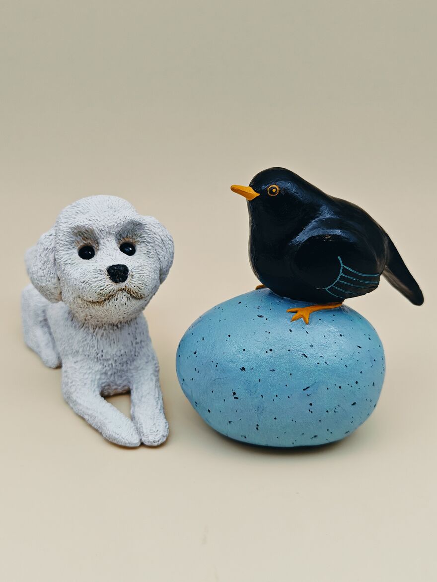 Two clay sculptures, one of a dog and the other of a bird on a large blue egg
