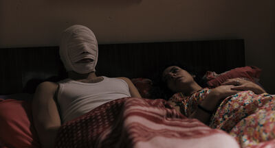 Two people in a bed, one with bandages on their head