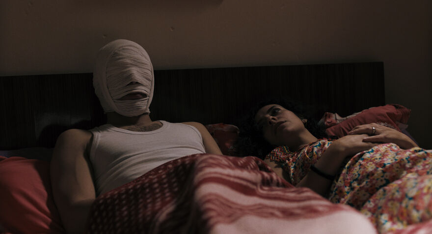 Two people in a bed, one with bandages on their head
