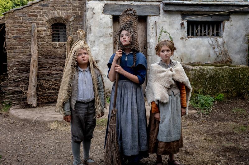 Three children in medieval clothing stand outside in a courtyard