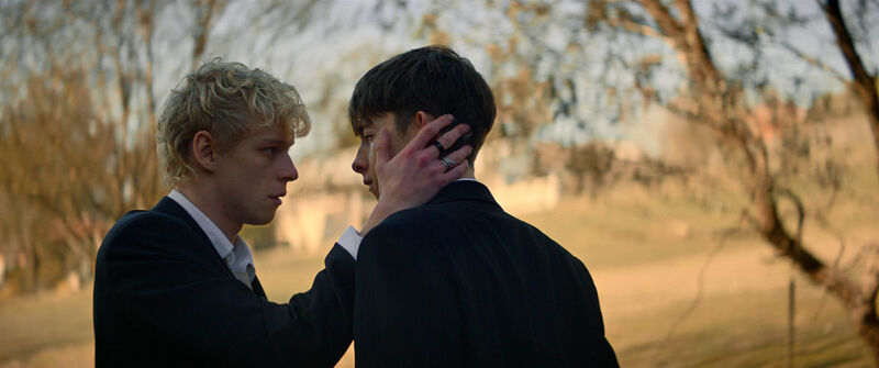 A blonde teenager cups another teenager's face in his hand