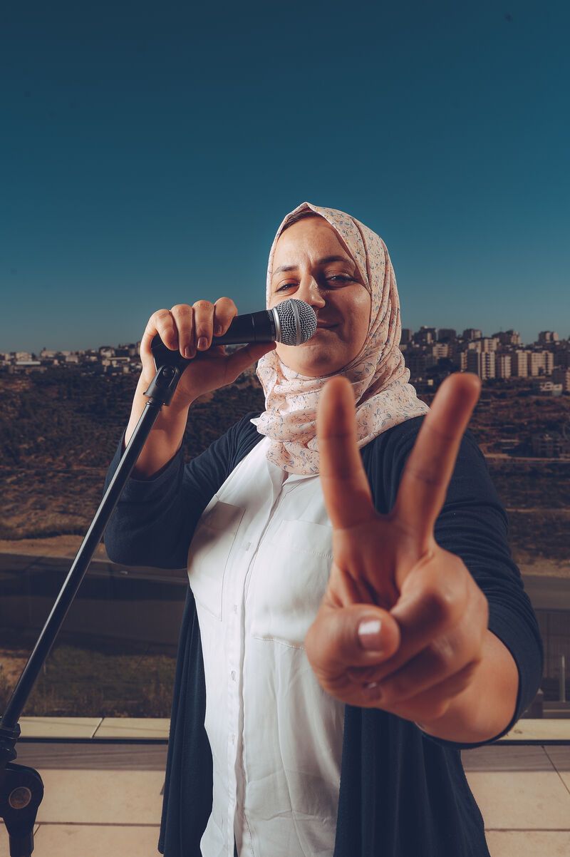 A woman holds a microphone and gives the peace sign