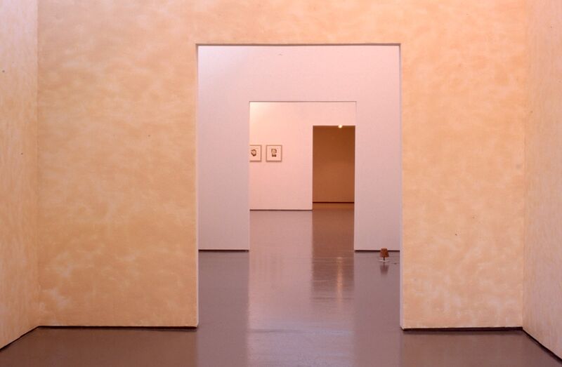A gallery wall is painted peach, with a square entrance. 